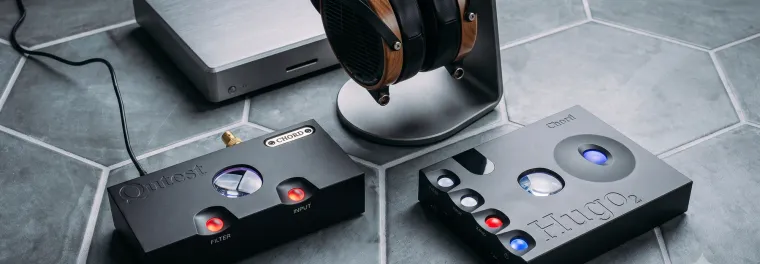 Chord Qutest and Hugo 2 side by side on a tiled floor with open-back headphones on a stand
